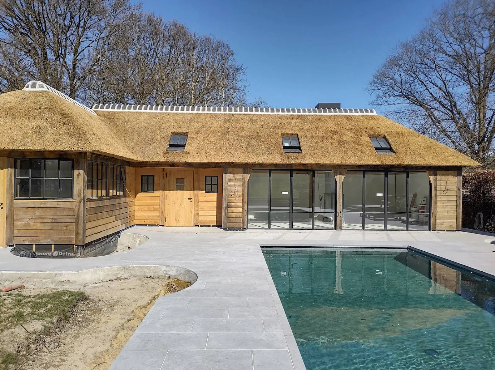 Poolhouse op maat in hout en staal met grote glaspartijen aan het zwembad